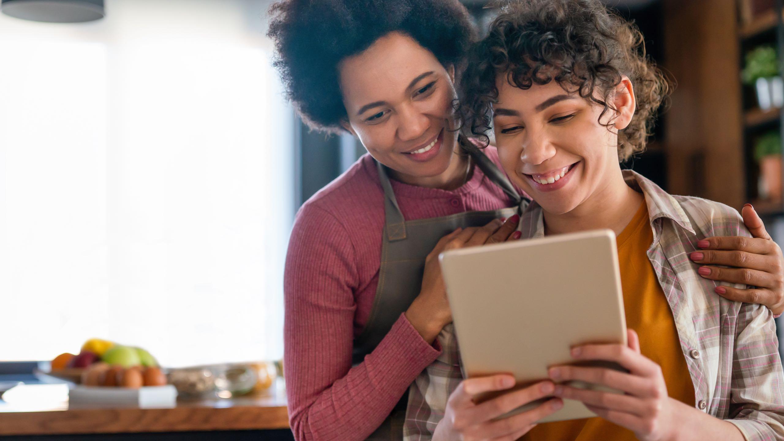 Happy multiethnic parents and kid having fun while cooking and following recipe on the internet.