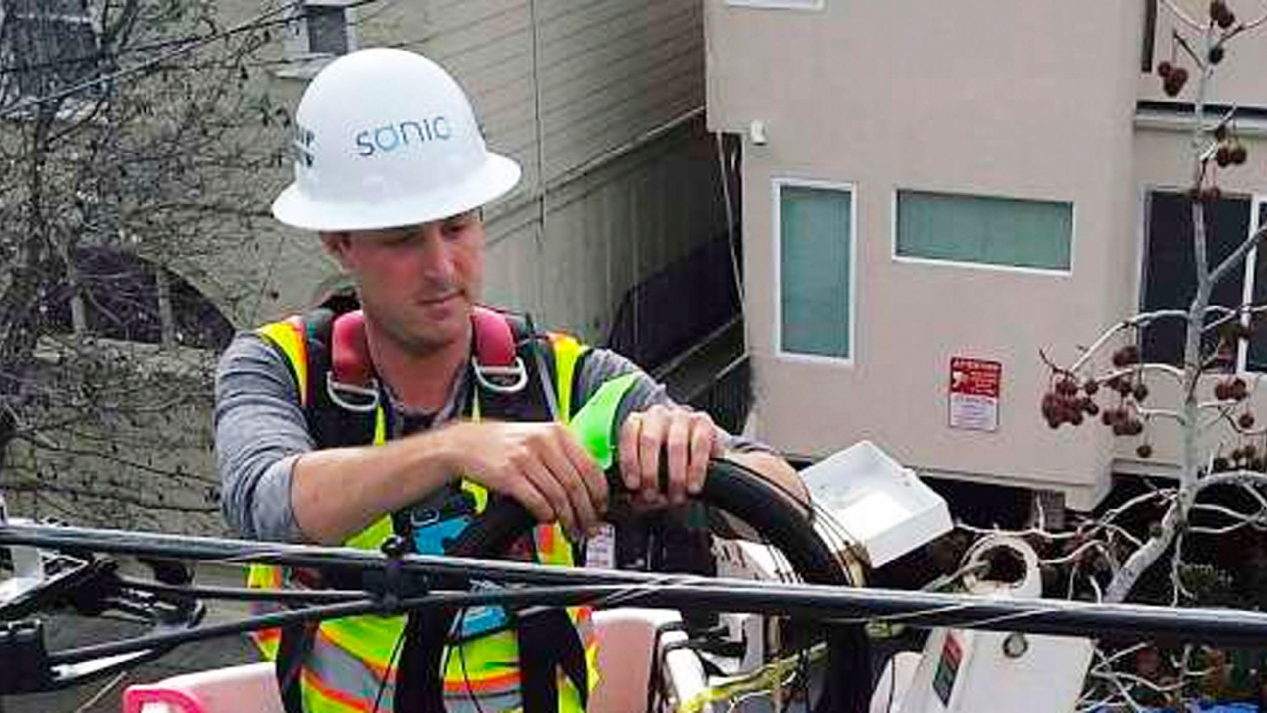 Sonic technician Tom Sherrill works on securing the cable to the utility wires through branches as he installs fiber optic cable in Berkeley.